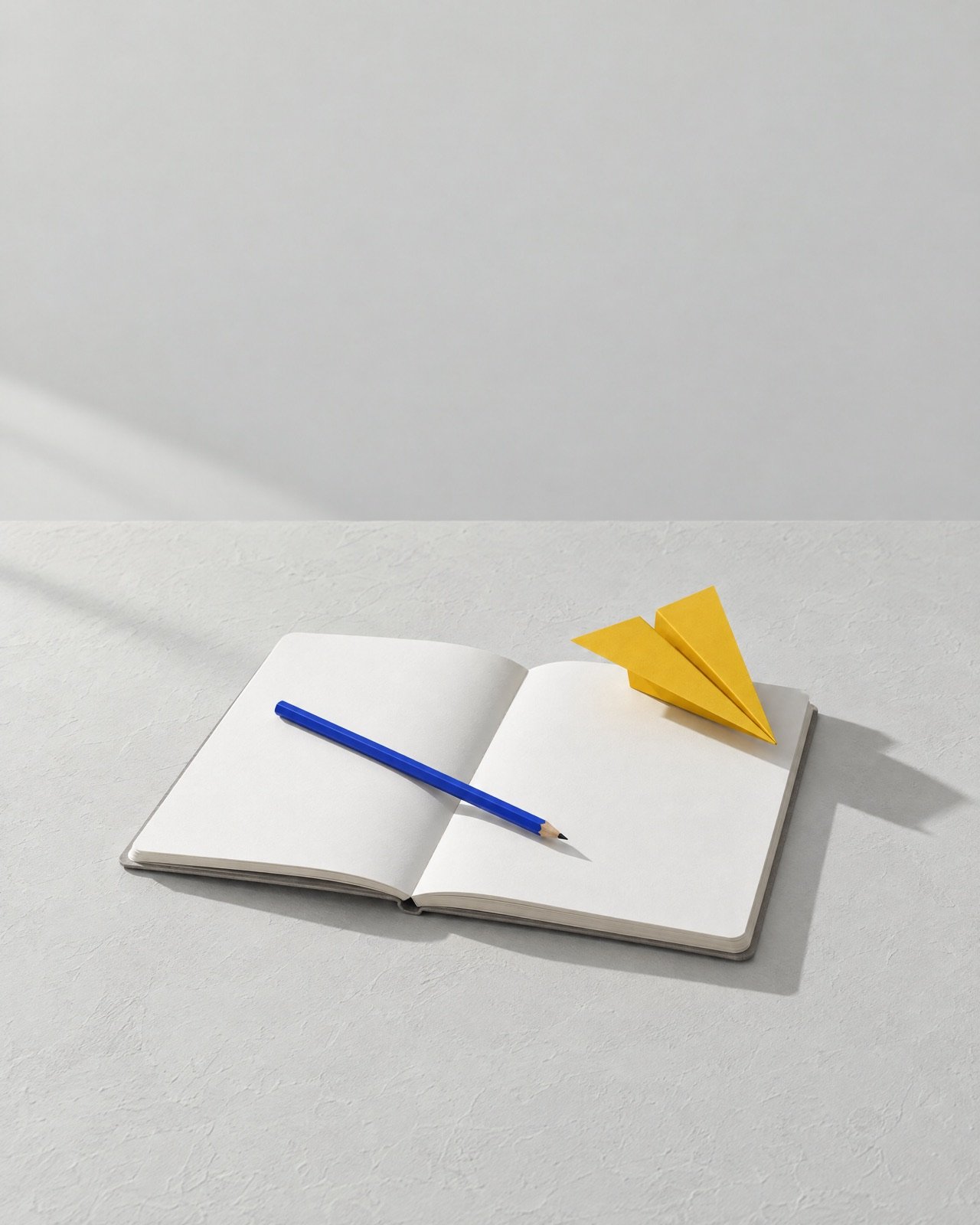 An open blank notebook with a blue pencil and a yellow paper plane